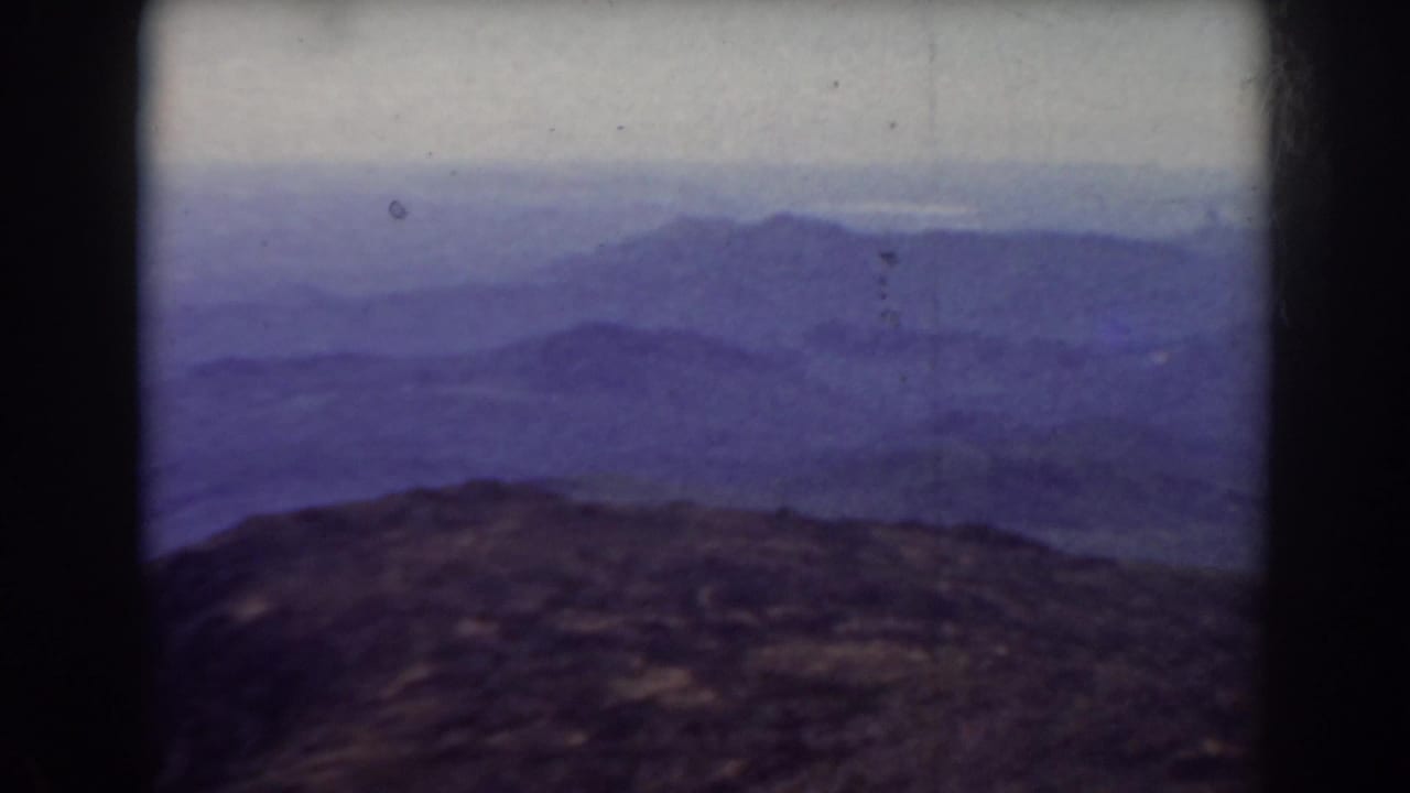 Distant mountain range and rocky summit foreground framed by dark vertical film borders.