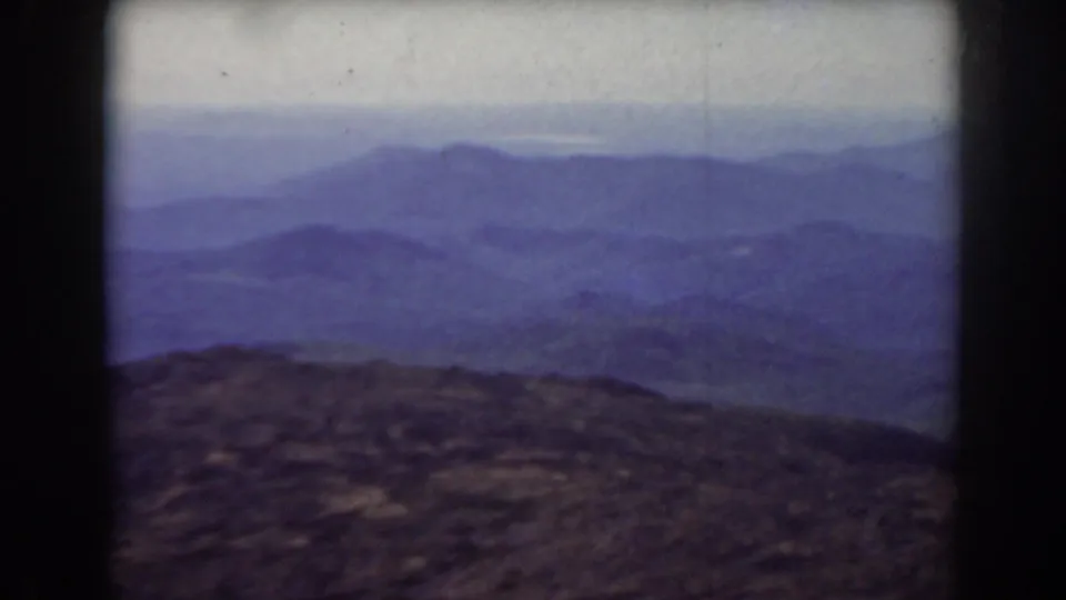 Vintage 8mm view from Mount Washington showing hazy blue ridges and dark foreground rock across a softly exposed frame.