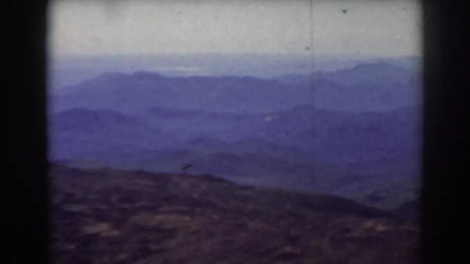 1938 Mount Washington landscape frame with layered ridges, muted purple-blue color, rocky foreground, and visible film wear.