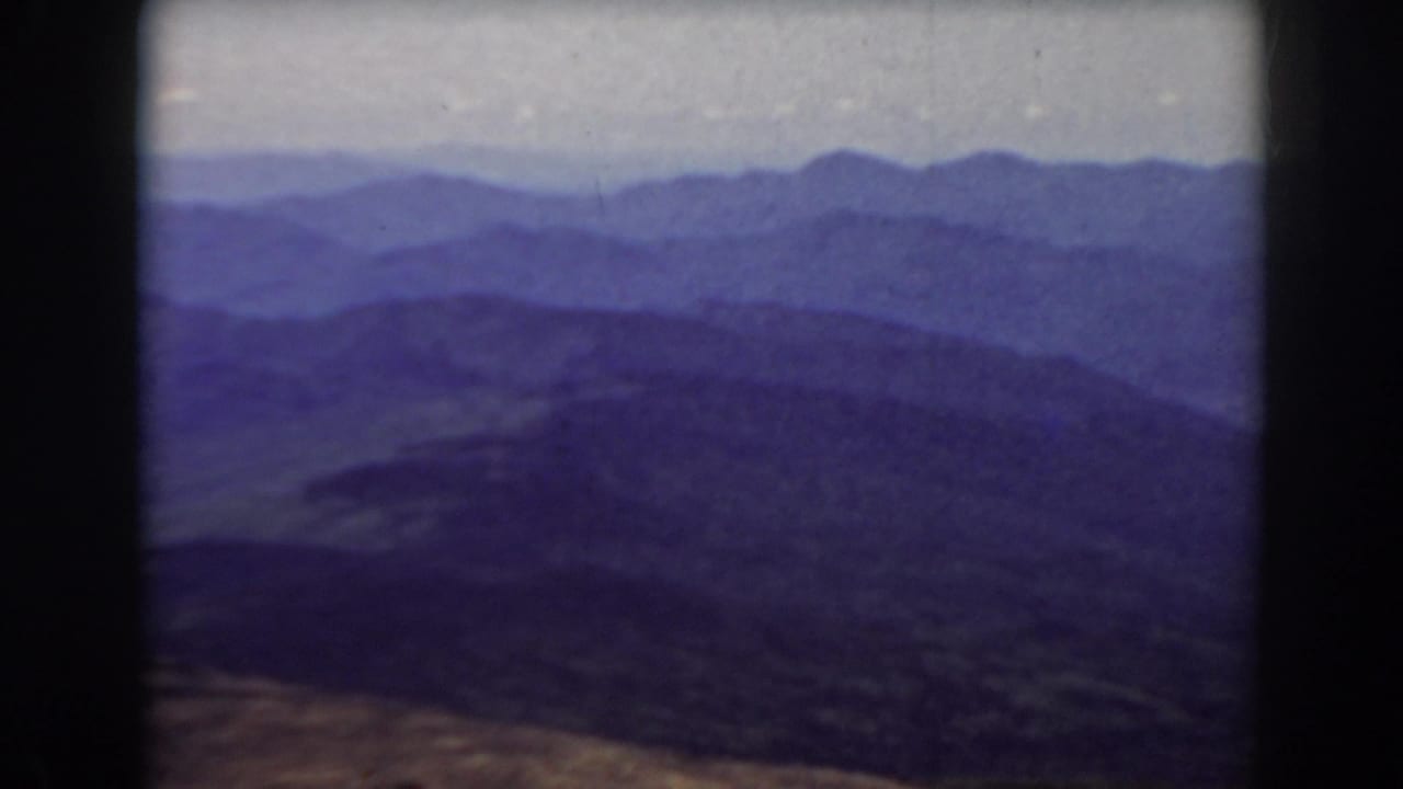 Distant mountain ranges and wooded slopes seen through a dark film border.