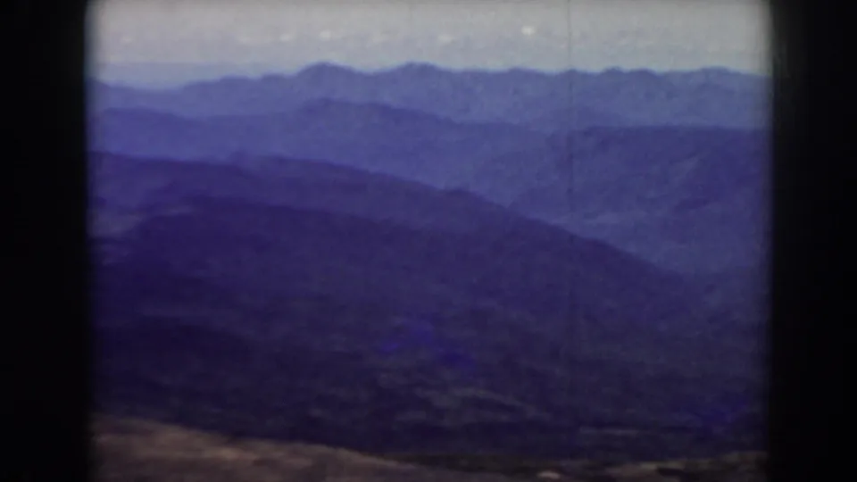 1938 Mount Washington-area home-movie frame showing layered New Hampshire mountain ridges with a pale sky and blue-purple film cast.