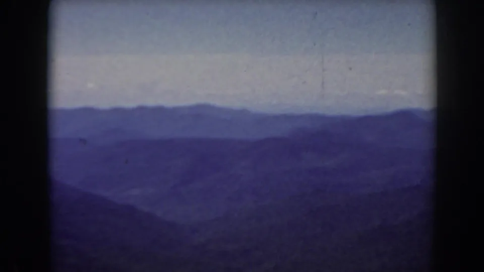 Mount Washington-area 8mm frame showing distant New Hampshire ridges, valley haze, pale sky, and strong blue-purple film color.