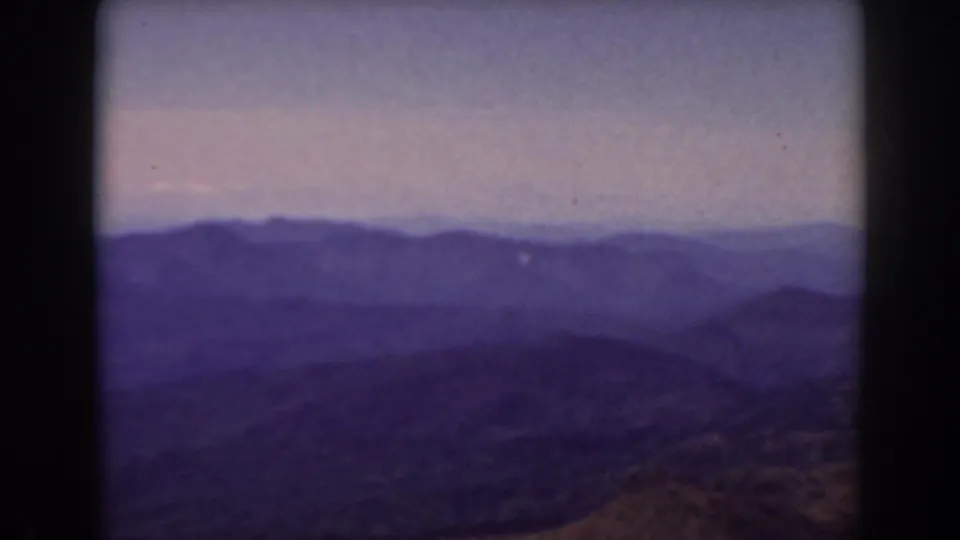 1938 Mount Washington area view with silhouetted mountain ridges, subdued sky, and brown rolling fields in the foreground.
