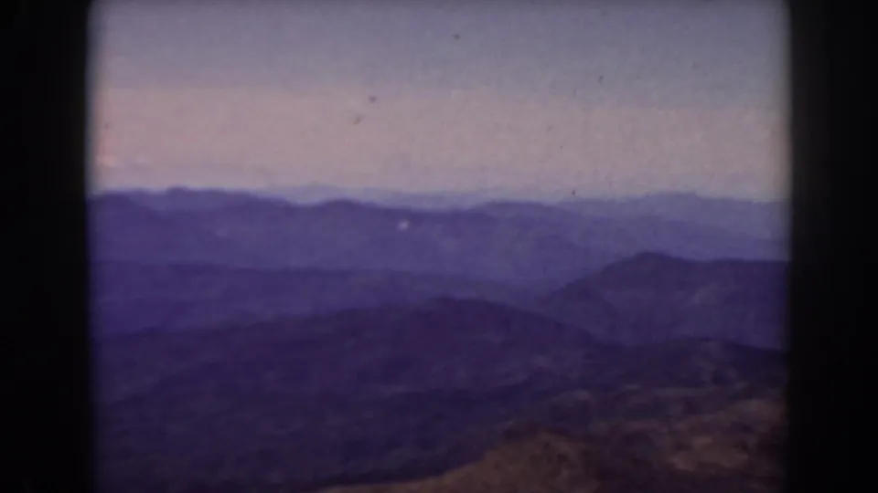 1938 Mount Washington home-movie frame showing distant New Hampshire mountain ridges through soft haze and purple-blue color cast.