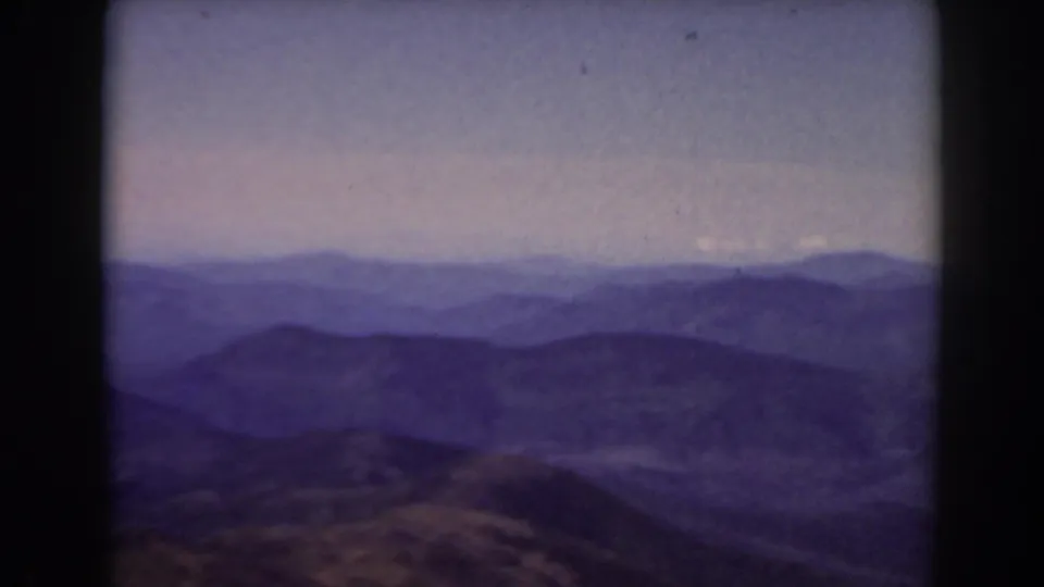 Vintage 8mm frame from Mount Washington showing broad New Hampshire ridgelines fading into a pale, hazy sky.