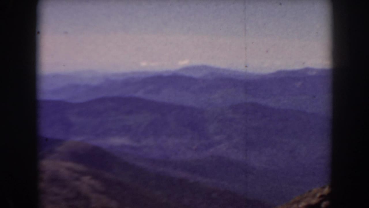 Layered mountain ridges under a pale sky with dark film borders.