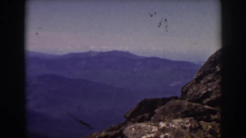 Mount Washington overlook with rocks in the foreground and hazy New Hampshire ridges beyond.