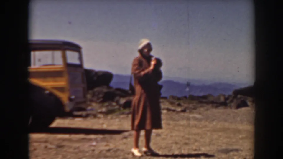 At Mount Washington in 1938, a woman stands near a wood-paneled car while facing the mountain panorama.