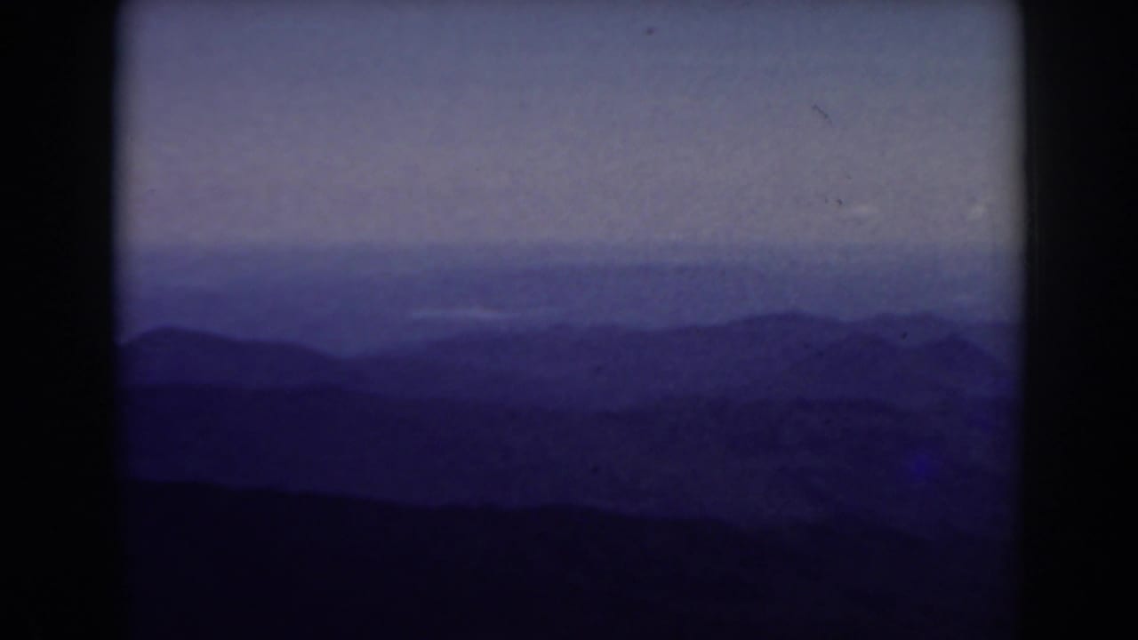 Distant blue mountain ridges beneath a pale hazy sky with dark 8mm frame borders.