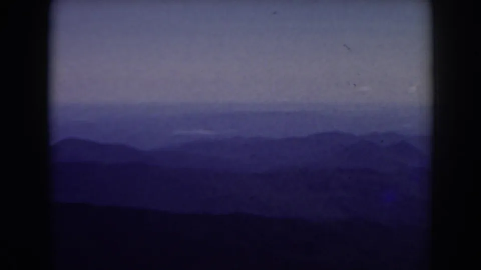 1938 Mount Washington home-movie frame showing layered New Hampshire mountain ridges in blue-purple haze under a pale sky.
