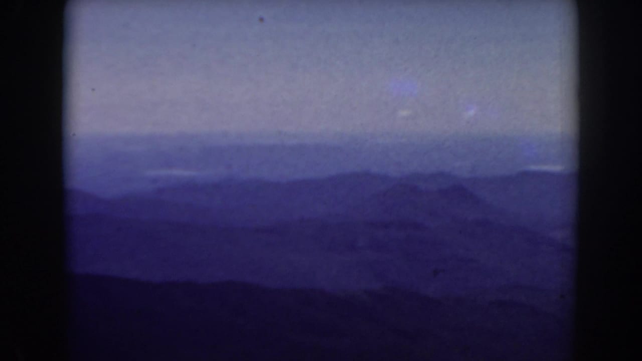 Blue mountain range receding into haze beneath a muted sky, framed by dark film edges.