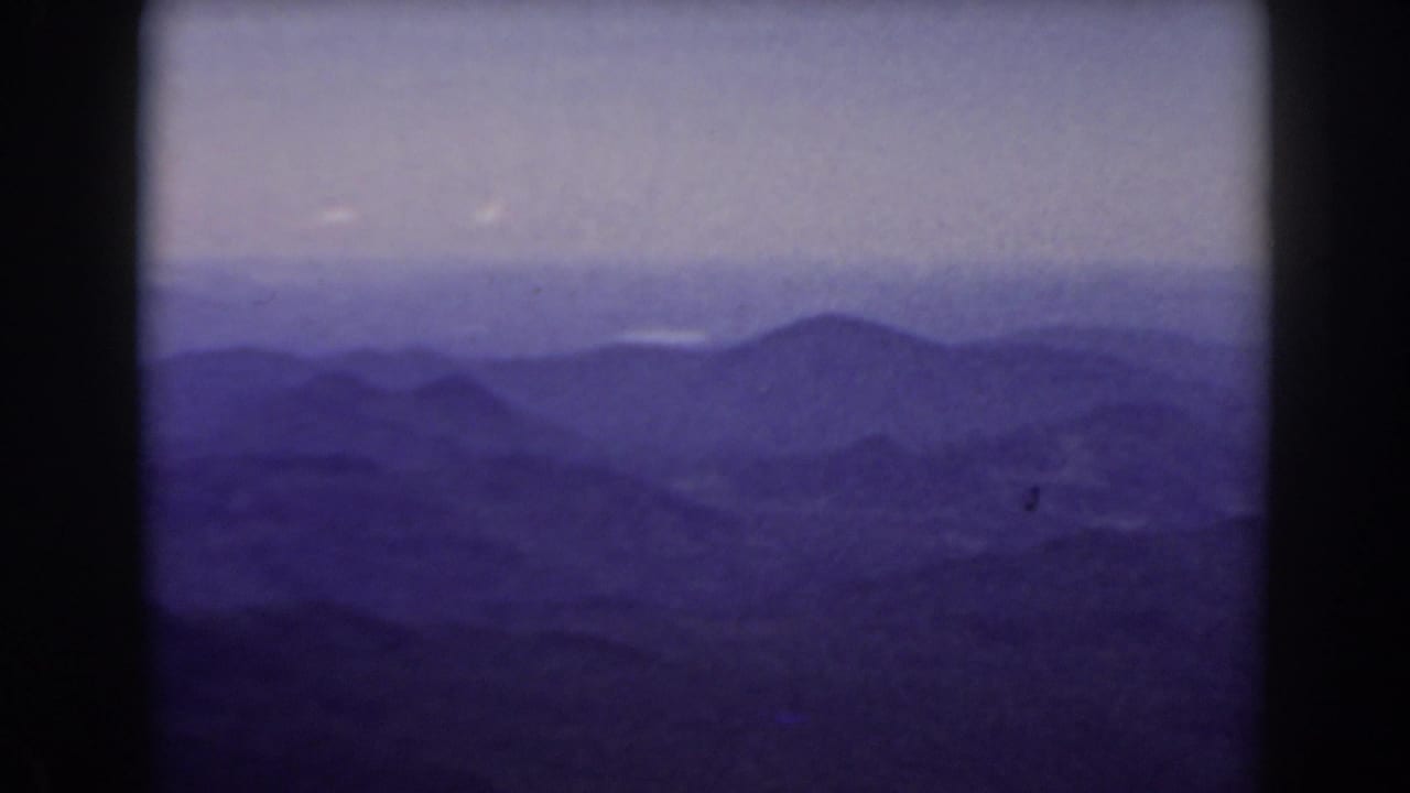 Hazy layered mountain ranges under a pale sky with dark 8mm frame borders.