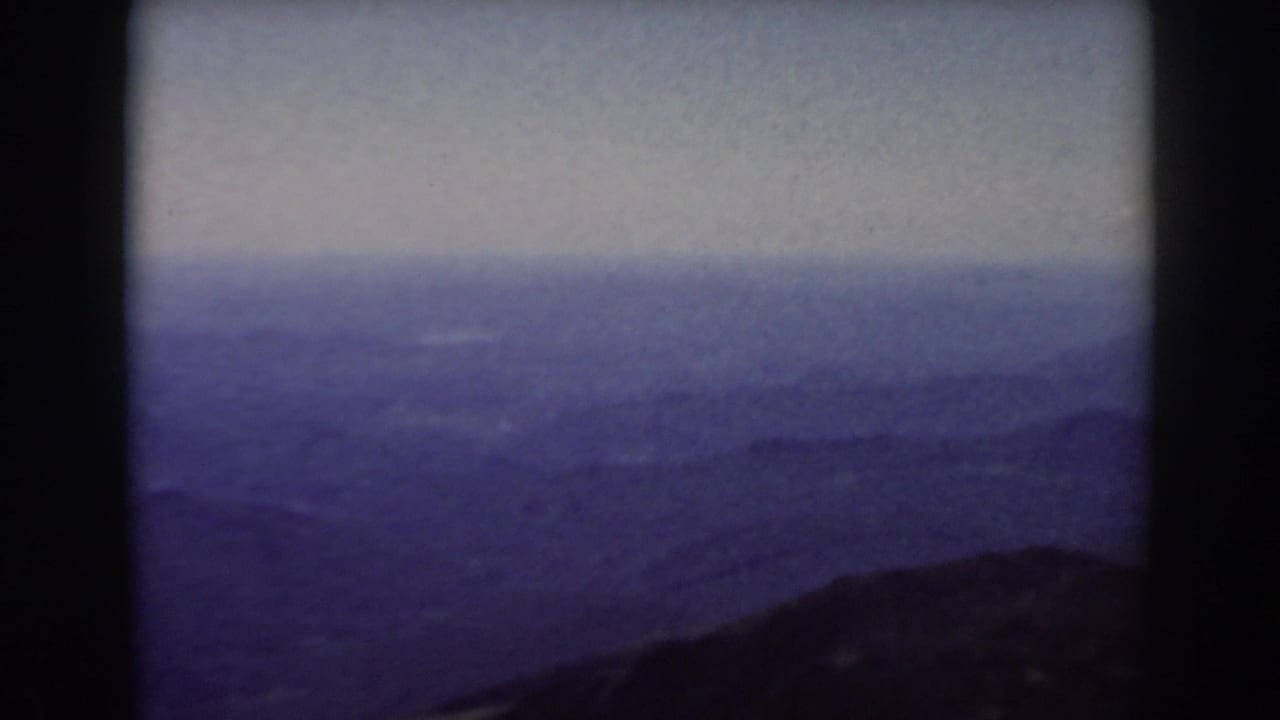 Mount Washington home-movie frame showing a soft, purple-toned panorama of distant New Hampshire mountains.
