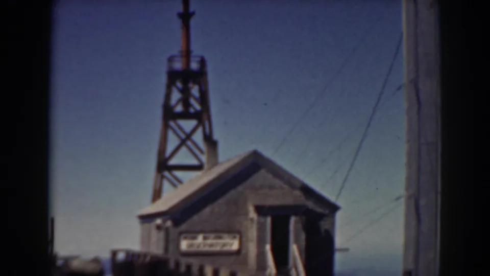 The 1938 home-movie frame looks toward a small Mount Washington trackside building, with a tower overhead and railroad bridge details in view.