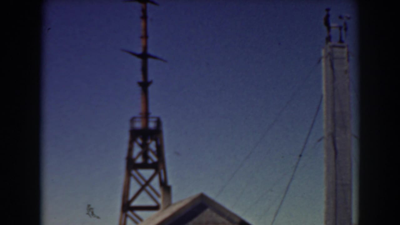 Tower and tall pole above a small wooden structure against a blue sky.