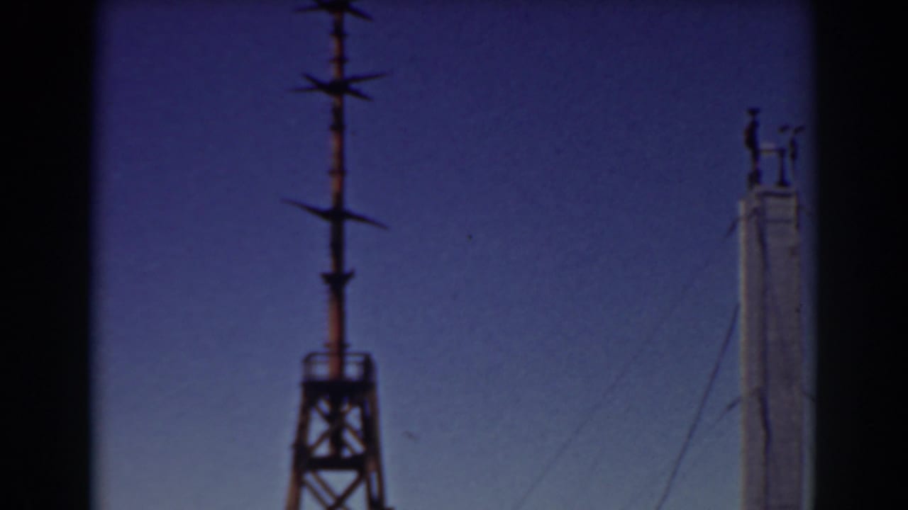 Tall pole with small workers near the top and wires against the sky.