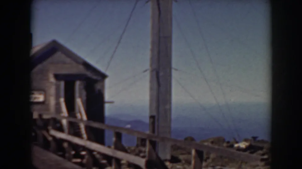 Mount Washington 8mm frame with a wooden building, fence, tall pole, guy wires, rocky ground, and distant mountain terrain.