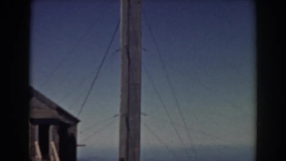A tall wired pole dominates the Mount Washington view, with a small building, blue sky, and hazy mountain horizon below.
