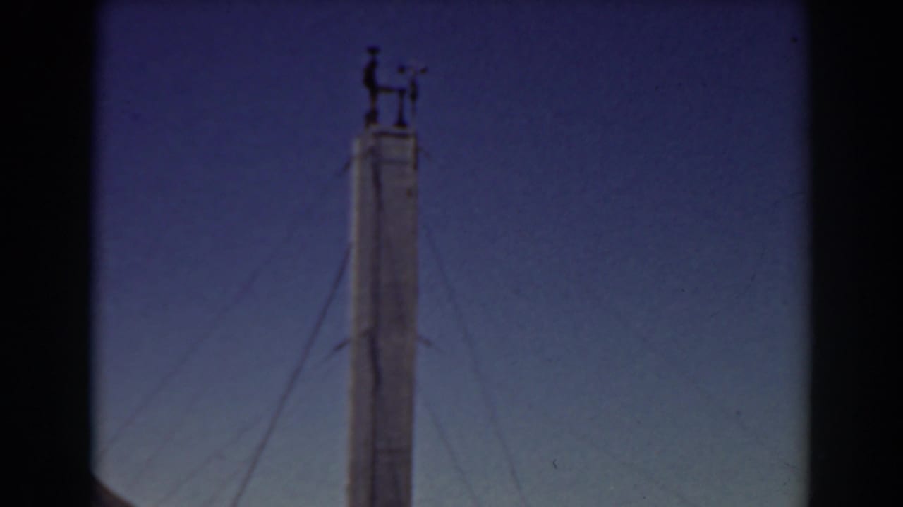 Top of a tall tower with wind-vane hardware silhouetted against the sky.