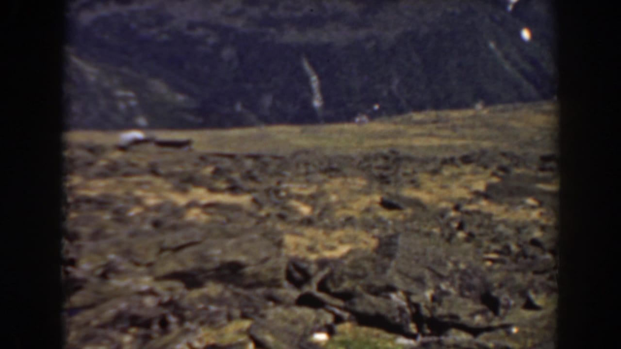Rocky mountain terrain with dry grass and a distant dark slope.