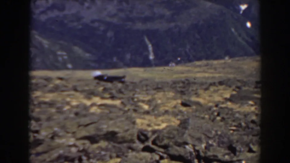 Mount Washington home-movie still with rough rocks, low grass, and a dark mountain slope beyond.