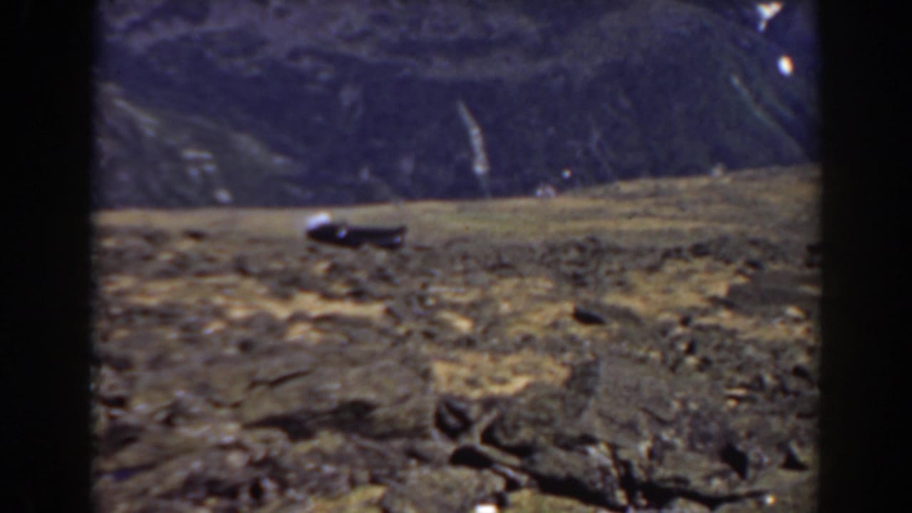 Small train on a rocky mountain slope with dark mountains in the background.