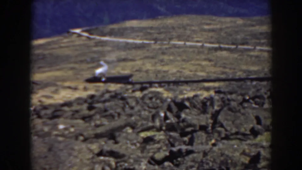 1938 Mount Washington frame with a small train giving off white smoke as it moves across a rocky mountain grade.