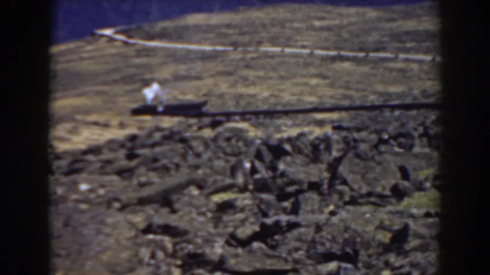 Mount Washington 1938 home-movie frame showing the smoking train farther along the track behind a rocky foreground.