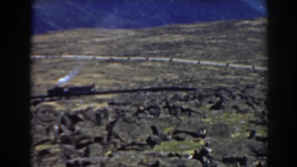 1938 Mount Washington home-movie frame showing a steam locomotive on a rocky mountain railway curve under blue sky.