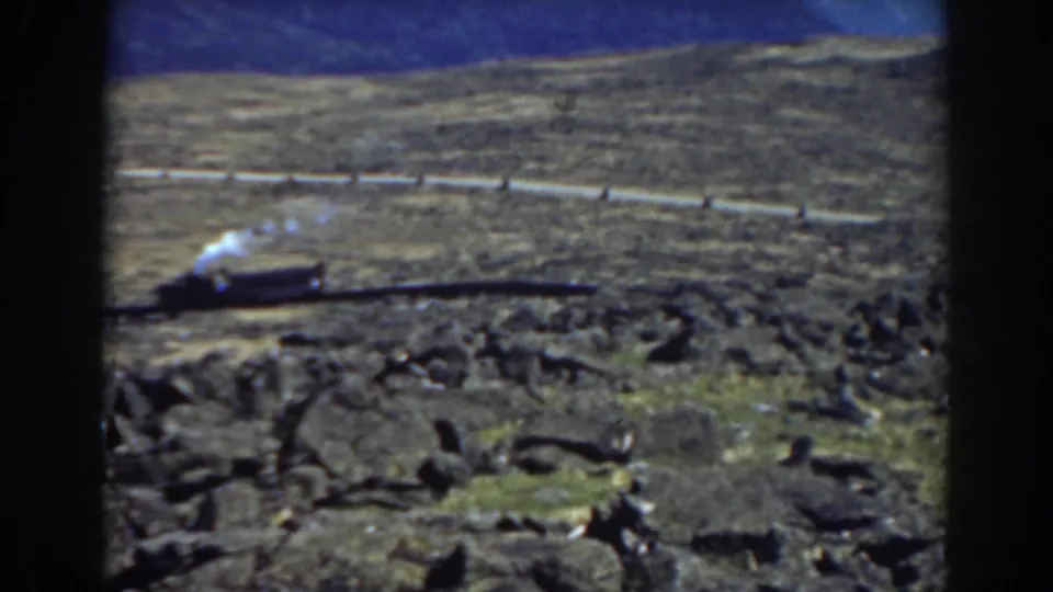 1938 Mount Washington frame with a steam train on the hillside track, rocky ground in front, and ridges behind.