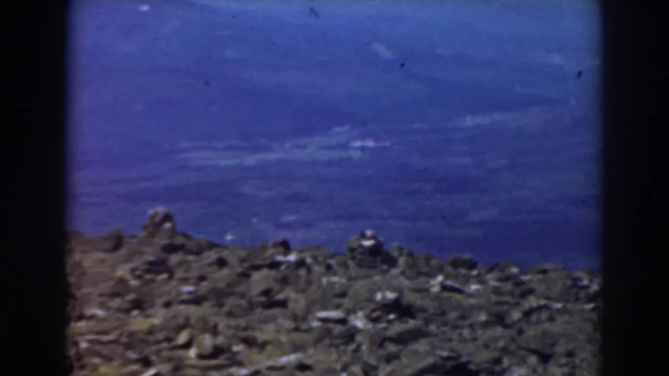 1938 Mount Washington travel-film frame looking across rocky summit foreground toward a hazy blue valley and distant mountain forms.