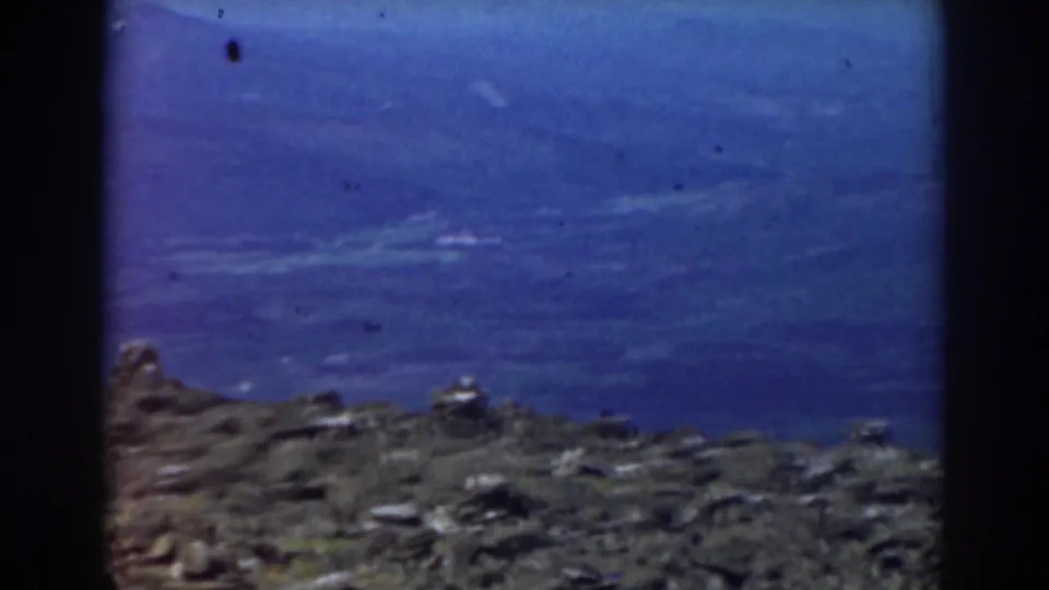 1938 Mount Washington home-movie frame showing a rocky foreground against a broad, dark blue sky with light cloud streaks.