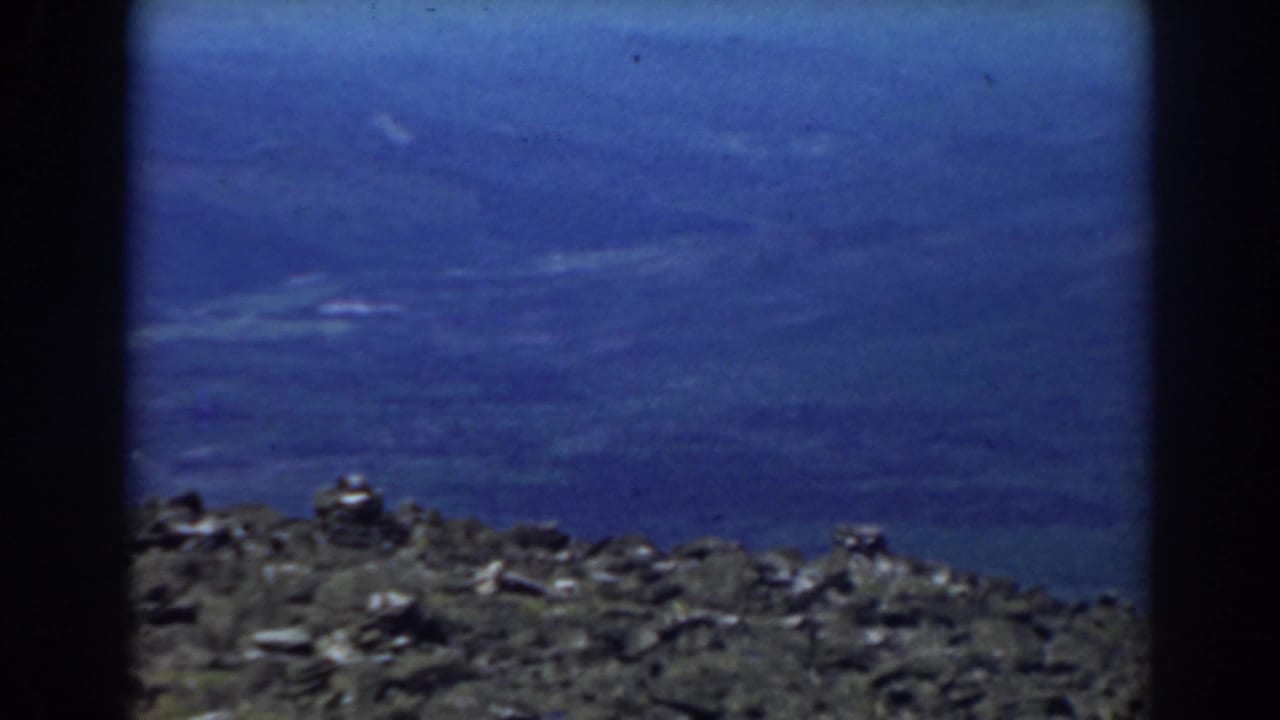 Rocky ridge line below a wide blue sky with soft haze and film gate edges.