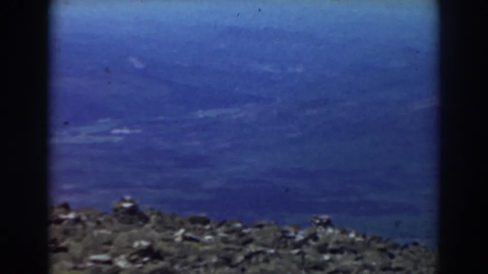 1938 Mount Washington frame with the rocky foreground dropping low beneath a broad blue sky and faint cloud texture.