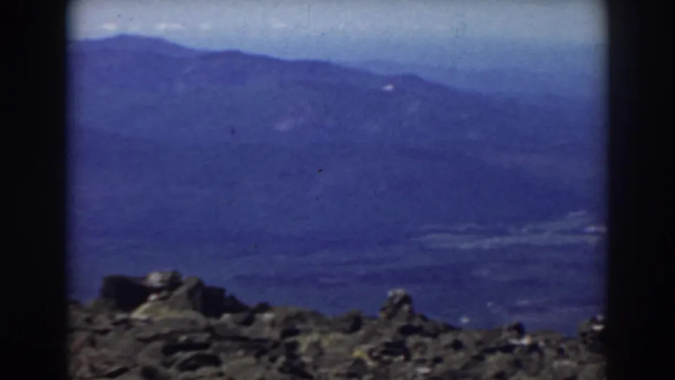 1938 Mount Washington home-movie frame with dark foreground rocks and distant hazy mountain terrain under a pale sky.