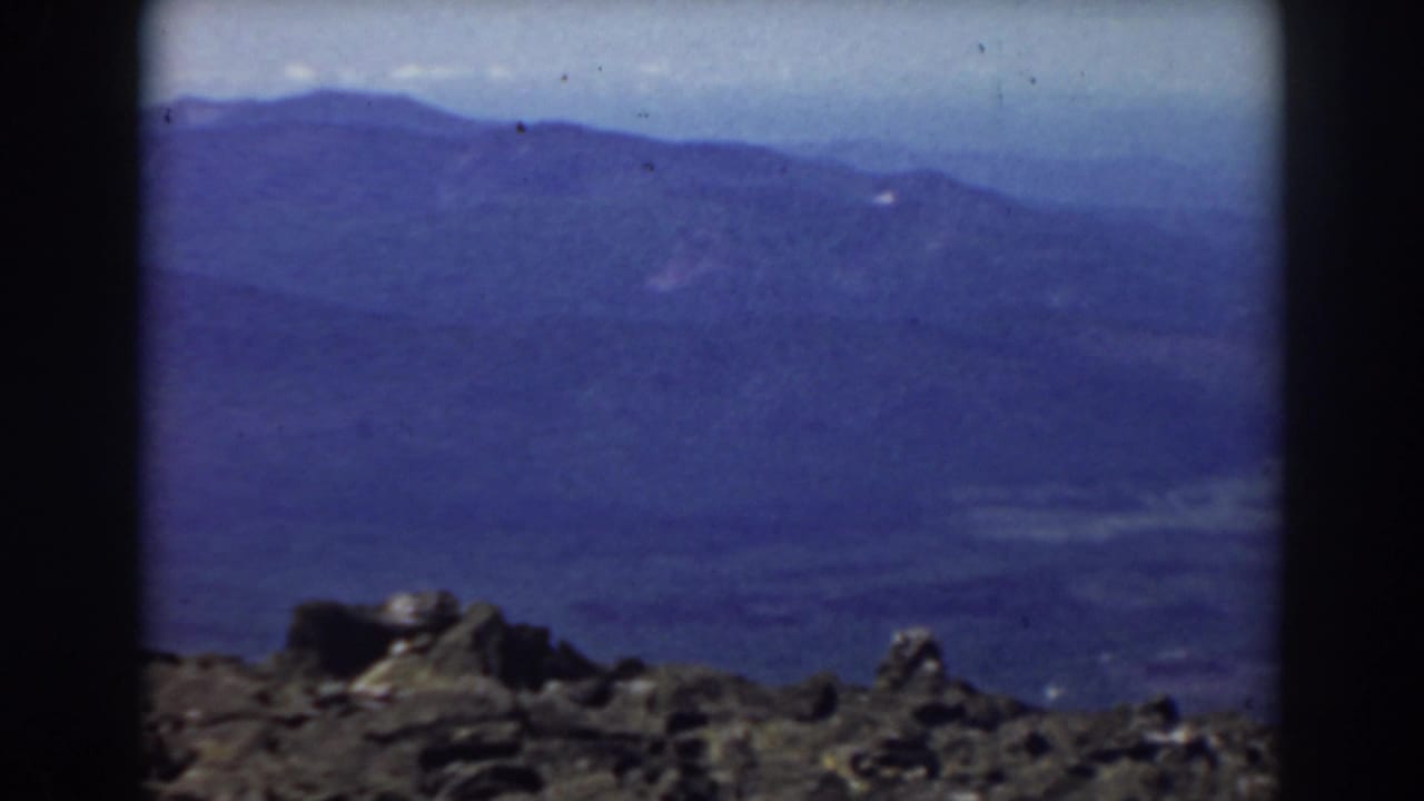 Rocky summit foreground with blue mountain ridges and pale sky beyond.