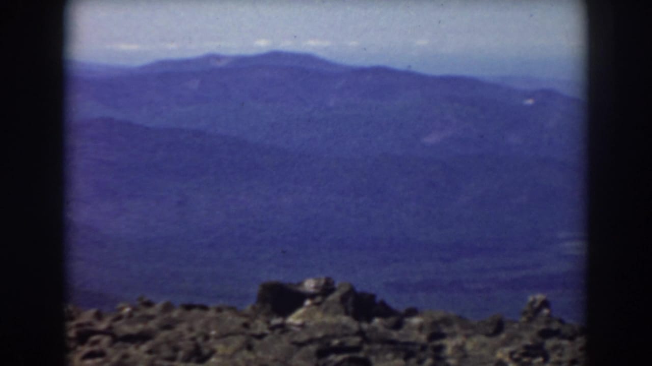 Mount Washington 8mm frame with a rocky overlook and layered blue mountain ridges fading into haze.