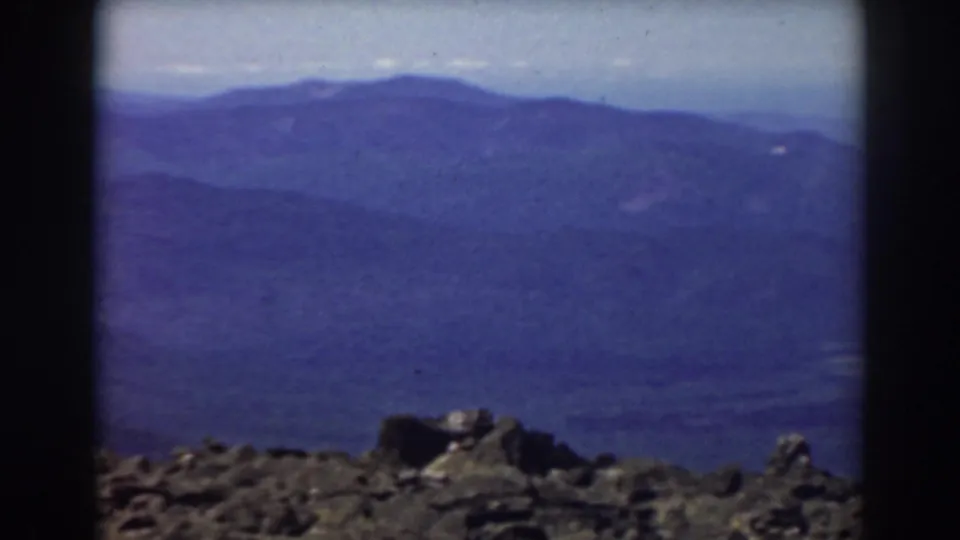 Mount Washington 8mm frame with a rocky overlook and layered blue mountain ridges fading into haze.