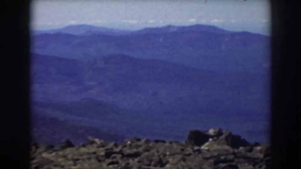 1938 New Hampshire mountain panorama from Mount Washington, with foreground rocks and soft blue ridgelines in the distance.