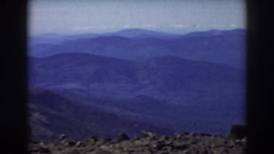8mm Mount Washington view showing rocky ground at the bottom of frame and distant New Hampshire mountain layers under pale sky.