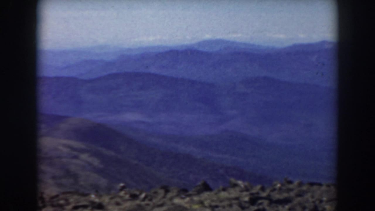 Layered blue mountain ranges seen beyond a rocky summit foreground.