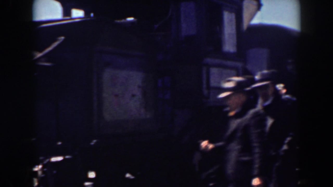 People pass beside a dark train car in shadow.