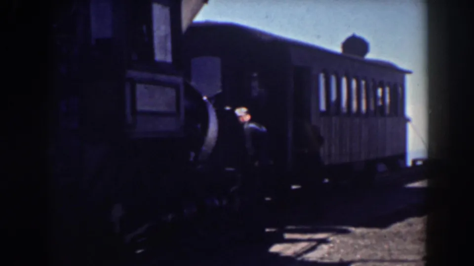 A rail worker stands by the passenger car as the train and platform area come into clearer daylight.