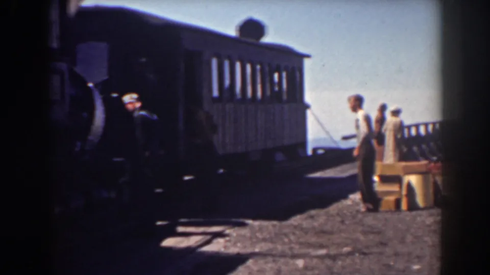 Travelers and a worker stand near luggage or crates beside the Mount Washington train car in bright daylight.