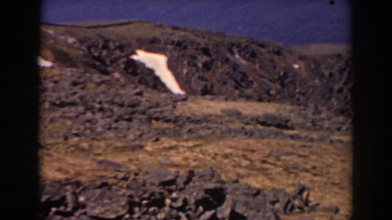 Rocky brown mountain slope with a white snow patch under blue sky.