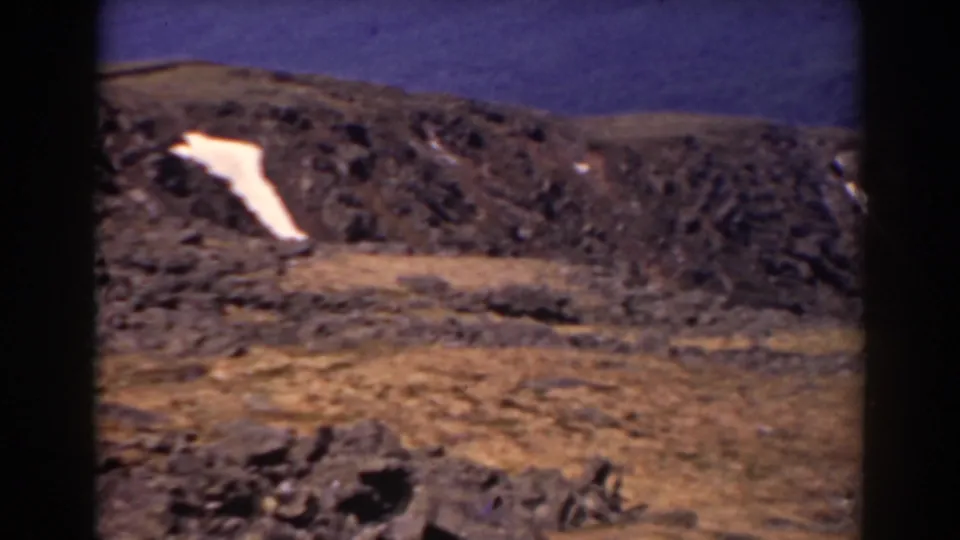 Archival 8mm view of Mount Washington terrain, showing a barren rocky slope, brown ground, and a small snow patch.