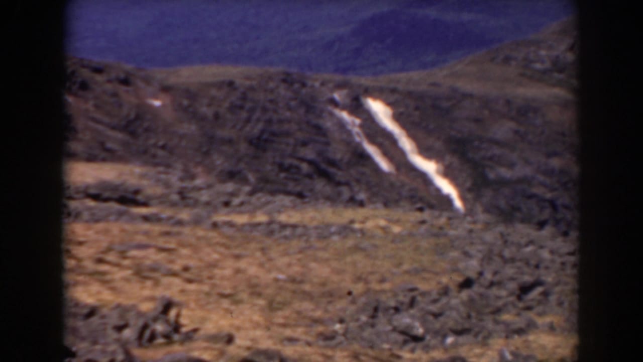 Rocky mountain slope with two bright snow patches and a dark film border.