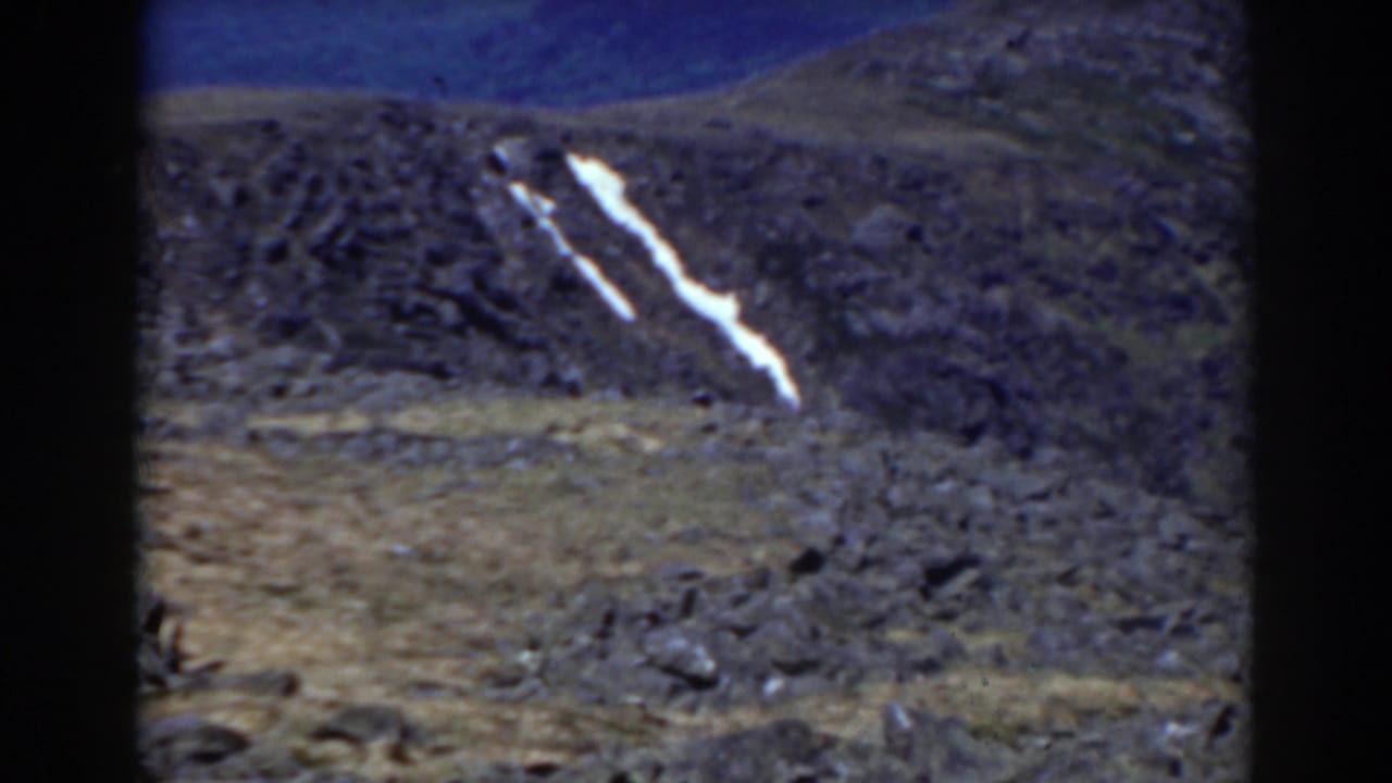 Barren rocky hillside with a long white snow patch below a blue sky.