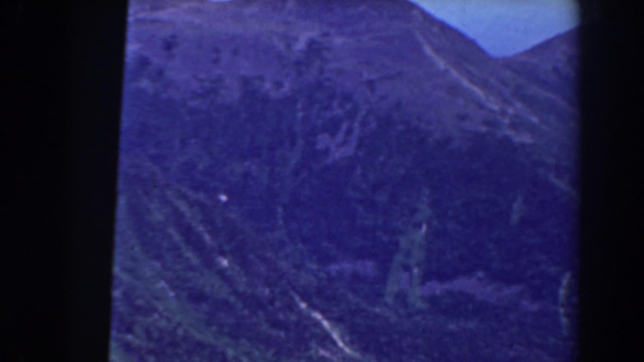 Forested mountain slope and dark film border, with blue sky above.