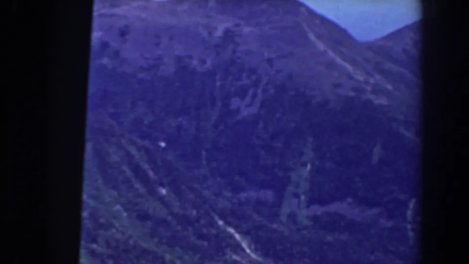 1938 Mount Washington-area 8mm frame showing a wooded mountain slope under blue sky, partly obscured by dark gate borders.